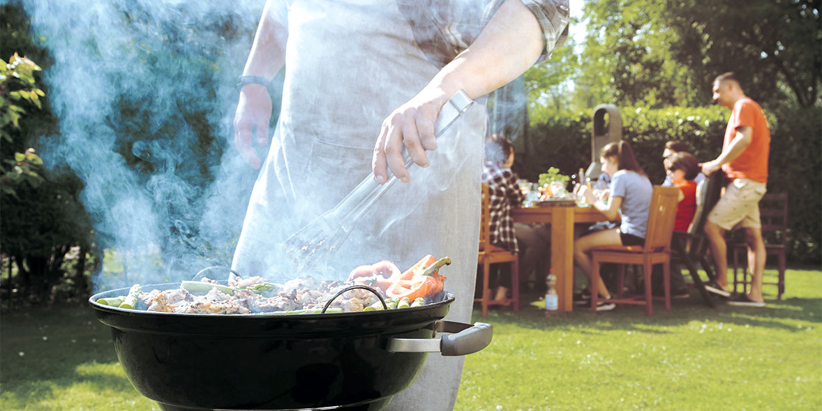 Someone cooking on a barbecue, with family including children sitting far away from the heat