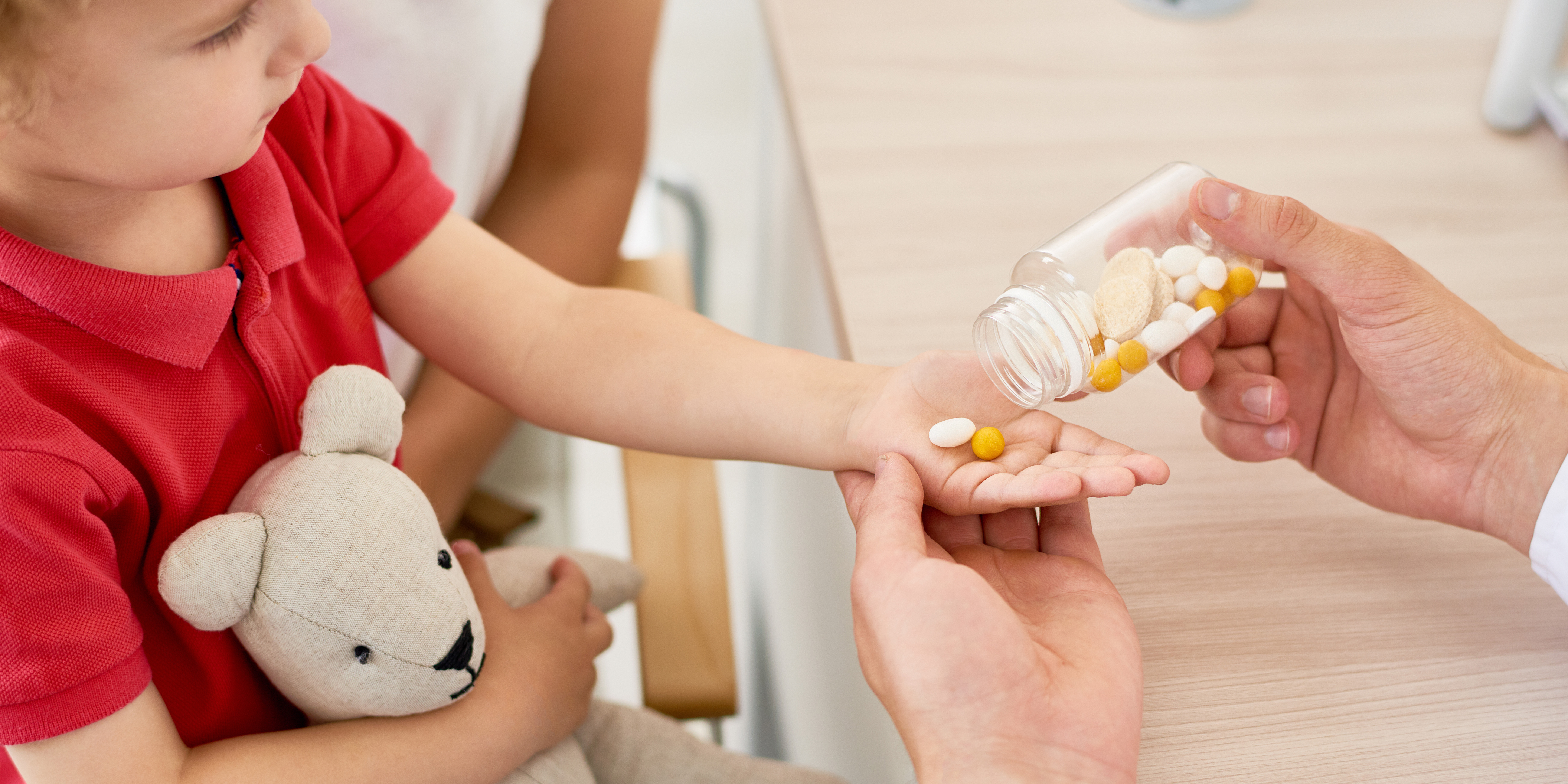 A child holding its hand out and being given supplements by an adult.